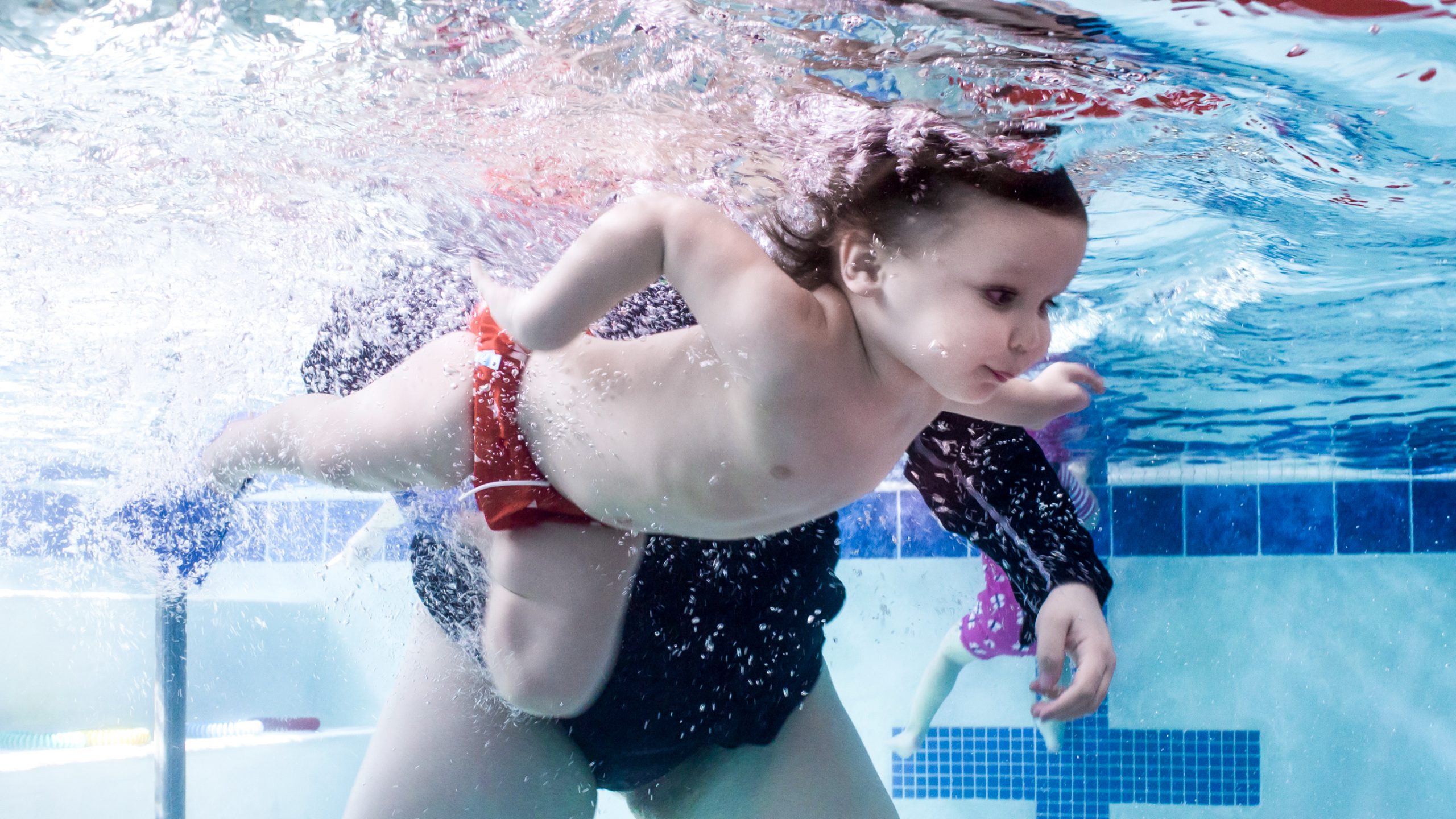 Toddler swimming independently across pool