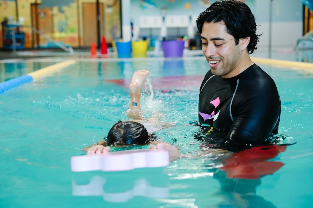 A man helping young swimmer with swimming aid in the pool