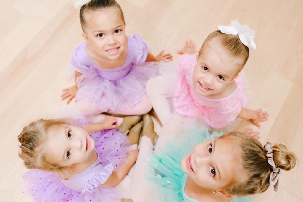 Four young smiling dancers looking up while sitting on dance floor.