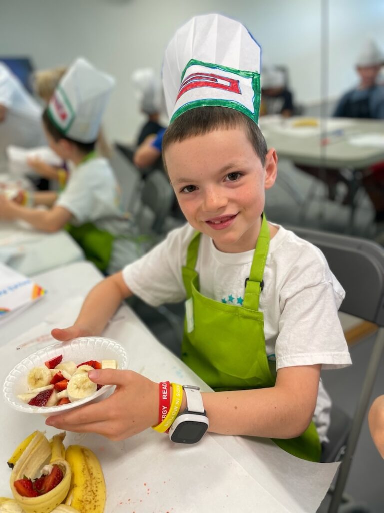Young boy with bowl of fruit and wearing chef hat.
