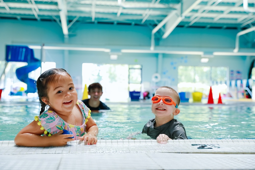Two smiling kids enjoying a swimming class at America's Kids In Motion.