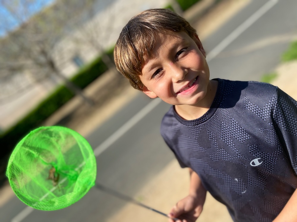 Smiling boy using a bug net during summer camp at America's Kids In Motion.