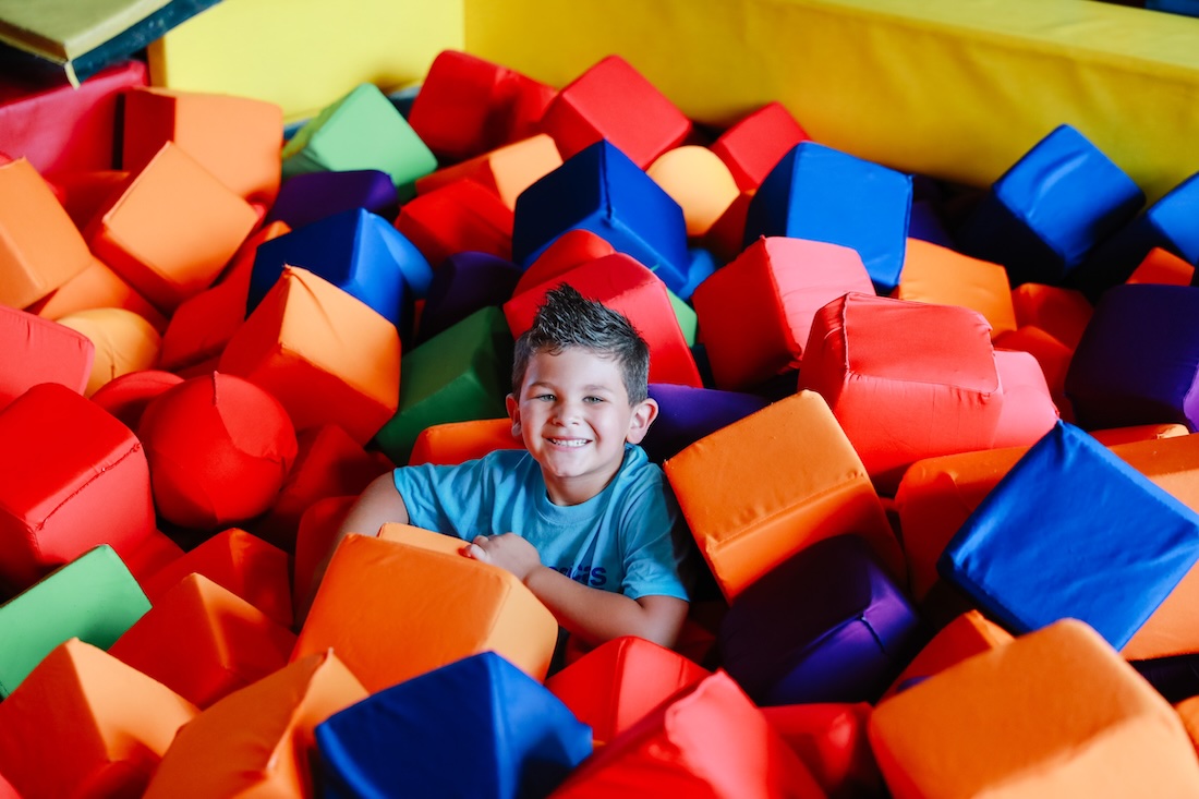 Smiling boy playing in a foam pit with multicolored blocks.