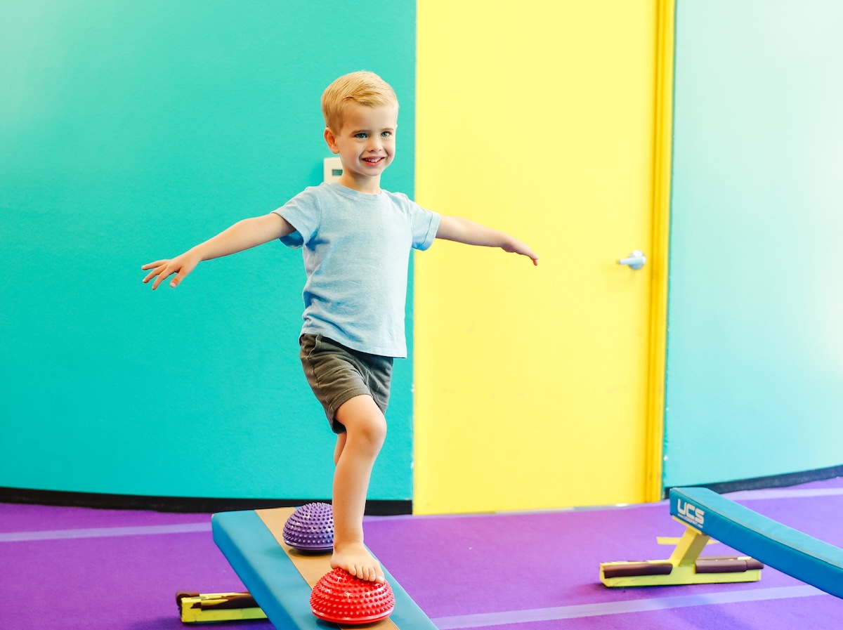 A young boy practicing on a balance beam during a boys' gymnastics class at AKIM.