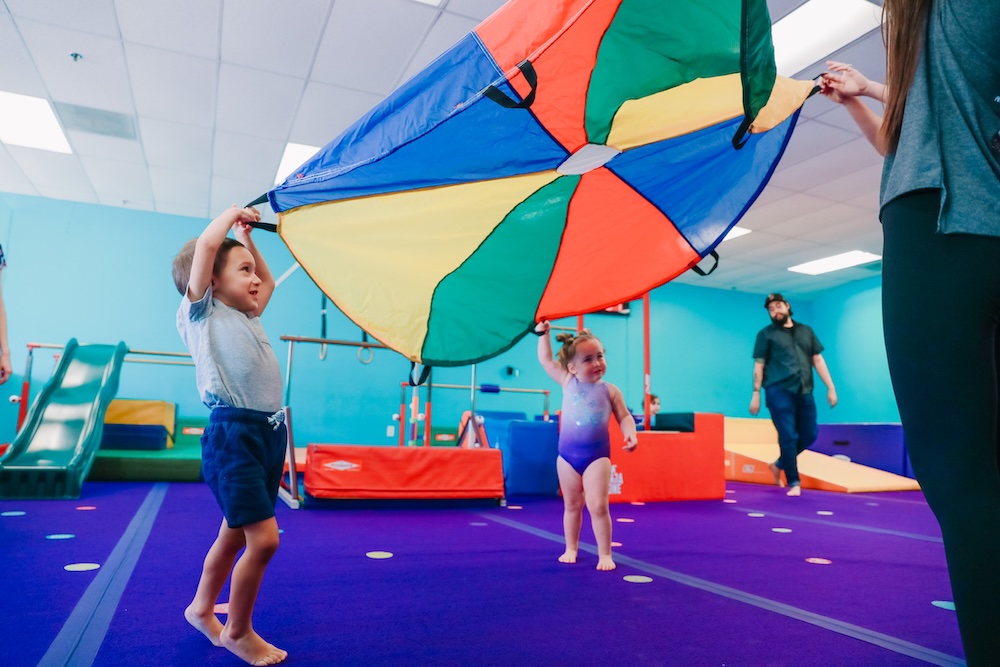 Kids playing indoors with a parachute during a class at America's Kids In Motion.