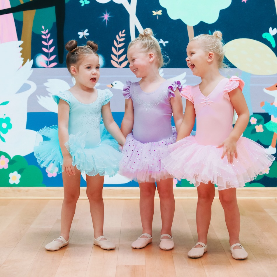 Three young ballerinas laughing together at preschool ballet class at AKIM.