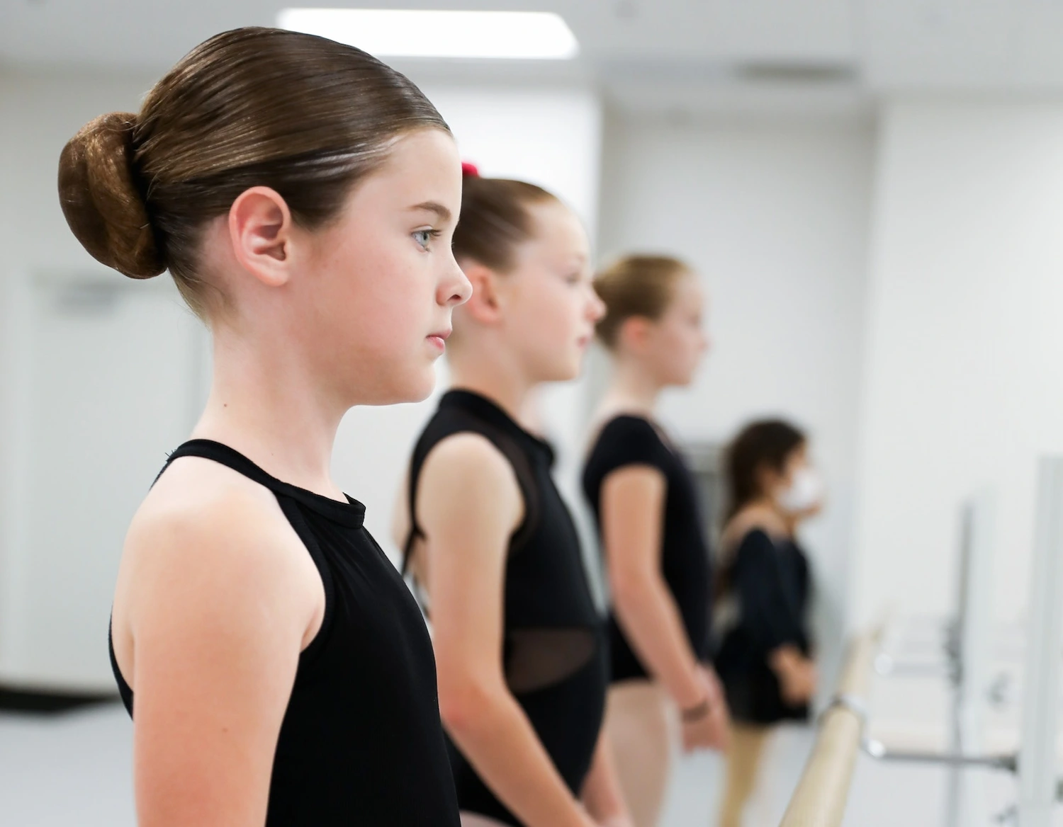 A group of girls standing at the bar in a ballet class at In the Spotlight dance studio.