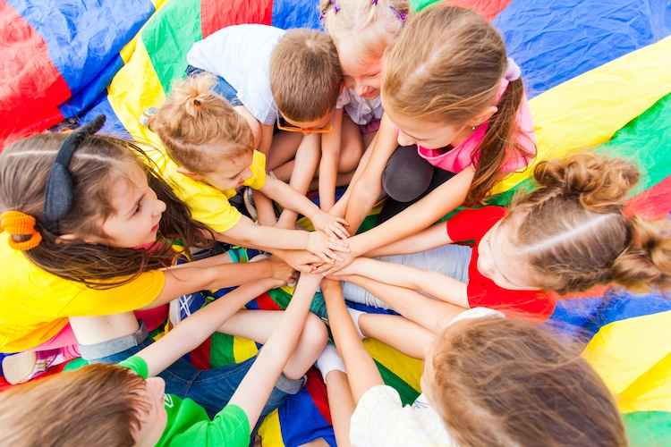 A group of kids putting their hands in a circle while playing on a parachute.