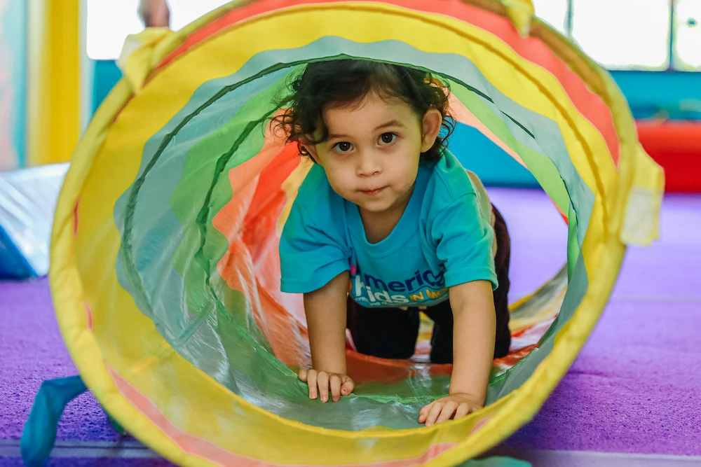 Young preschool student crawling through a colorful tube.