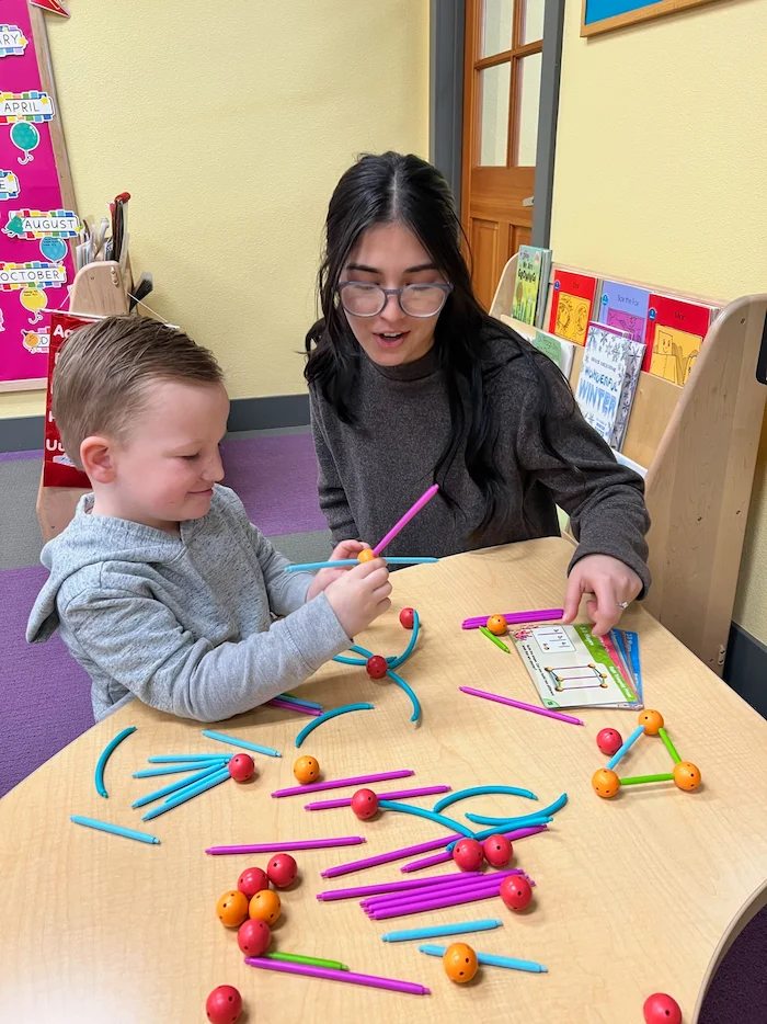 Pre-Kindergarten teacher working with a student at a table.